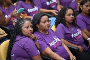 Portal Jaciara Barros – Mulheres vestindo camisetas roxas com o logotipo "força" sentaram-se lado a lado em auditório. – Portal Jaciara Barros