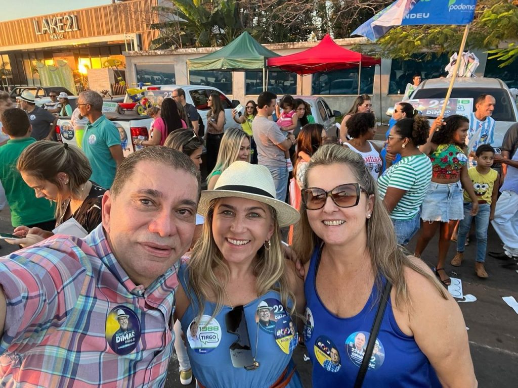 Portal Jaciara Barros – Três adultos tiram uma selfie em evento ao ar livre em Araguaína, com adesivos de campanha e tendas ao fundo. – Portal Jaciara Barros