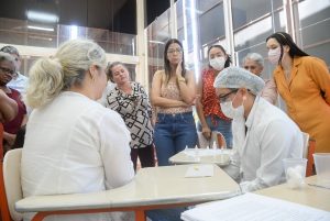 Portal Jaciara Barros – Enfermeiros das UPAs de máscara preparam testes de ISTs em uma mulher sentada, enquanto outras mulheres acompanham a cena. – Portal Jaciara Barros