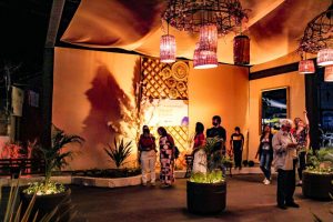 Portal Jaciara Barros – Pessoas caminham sob luzes pendentes à noite em espaço instagramável no Festival Gastronômico de Taquaruçu. – Portal Jaciara Barros