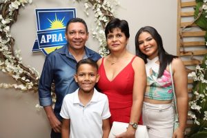 Portal Jaciara Barros – Quatro pessoas estão sorrindo diante de uma guirlanda de flores e um letreiro APRA soldado durante evento indoor. – Portal Jaciara Barros