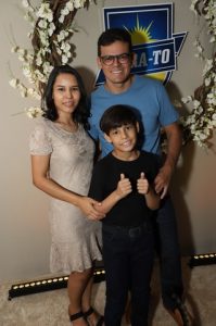 Portal Jaciara Barros – Em um ambiente interno, mulher, homem e menino posam diante de painel decorativo de soldado; o menino faz sinal positivo. – Portal Jaciara Barros