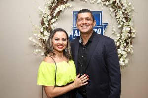 Portal Jaciara Barros – Uma mulher sorridente de blusa amarela posa ao lado de um soldado fardado, próximo a uma coroa de flores e uma placa. – Portal Jaciara Barros