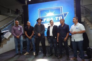 Portal Jaciara Barros – Seis homens, entre eles um soldado, posam diante de um grande telão com o logotipo PRA-TO em evento realizado em ambiente fechado. – Portal Jaciara Barros