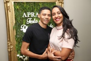 Portal Jaciara Barros – Um homem e uma mulher posam sorrindo juntos diante de um painel verde e dourado com tema de soldado. – Portal Jaciara Barros