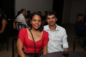 Portal Jaciara Barros – Durante um evento indoor, uma mulher de blusa vermelha e um homem trajado de soldado posam sorrindo para a câmera. – Portal Jaciara Barros