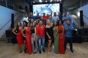 Portal Jaciara Barros – Um grupo, incluindo um soldado, posa sorrindo em escadaria interna iluminada, com uma placa ao fundo. – Portal Jaciara Barros