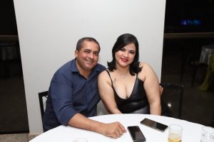 Portal Jaciara Barros – Um homem e uma mulher sentam-se juntos em uma mesa redonda, sorrindo enquanto conversam. Há bebidas e celulares sobre a mesa. – Portal Jaciara Barros