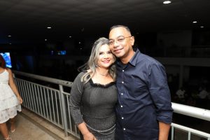 Portal Jaciara Barros – Uma mulher e um soldado posam juntos, sorrindo, em uma varanda interna com iluminação ambiente baixa ao fundo. – Portal Jaciara Barros