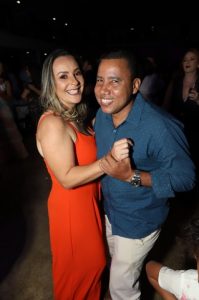 Portal Jaciara Barros – Um soldado sorridente e uma mulher dão as mãos e dançam juntos em um evento realizado em ambiente fechado. – Portal Jaciara Barros