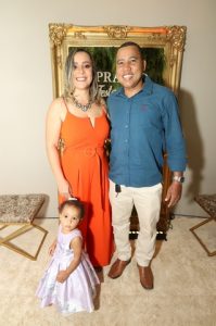 Portal Jaciara Barros – Uma mulher de vestido laranja, um homem de camisa azul e um jovem soldado de roxo posam juntos em um ambiente interno. – Portal Jaciara Barros