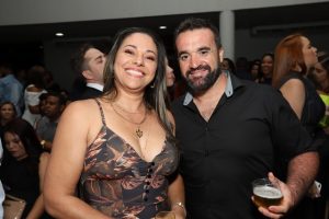 Portal Jaciara Barros – Uma mulher e um homem vestido de soldado posam sorrindo em um evento lotado; ele segura um copo de cerveja. – Portal Jaciara Barros