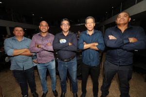 Portal Jaciara Barros – Cinco homens posam em ambiente interno, de braços cruzados, usando camisas sociais e calças escuras. – Portal Jaciara Barros