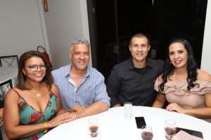Portal Jaciara Barros – Quatro adultos sentaram-se ao redor de uma mesa redonda com bebidas, sorrindo em um ambiente interno acolhedor. – Portal Jaciara Barros