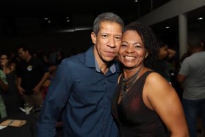 Portal Jaciara Barros – Um homem e uma mulher, sendo um deles fantasiado de soldado, estão sorrindo para a câmera em um local interno movimentado. – Portal Jaciara Barros