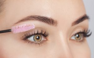 Portal Jaciara Barros – Pessoa utiliza escovinha rosa para pentear as sobrancelhas primavera bem cuidadas em close nos olhos. – Portal Jaciara Barros