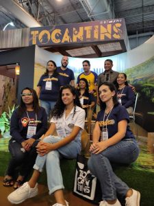 Portal Jaciara Barros – Alessandra Araújo posa para foto com um grupo no estande do Tocantins durante evento realizado em ambiente interno. – Portal Jaciara Barros