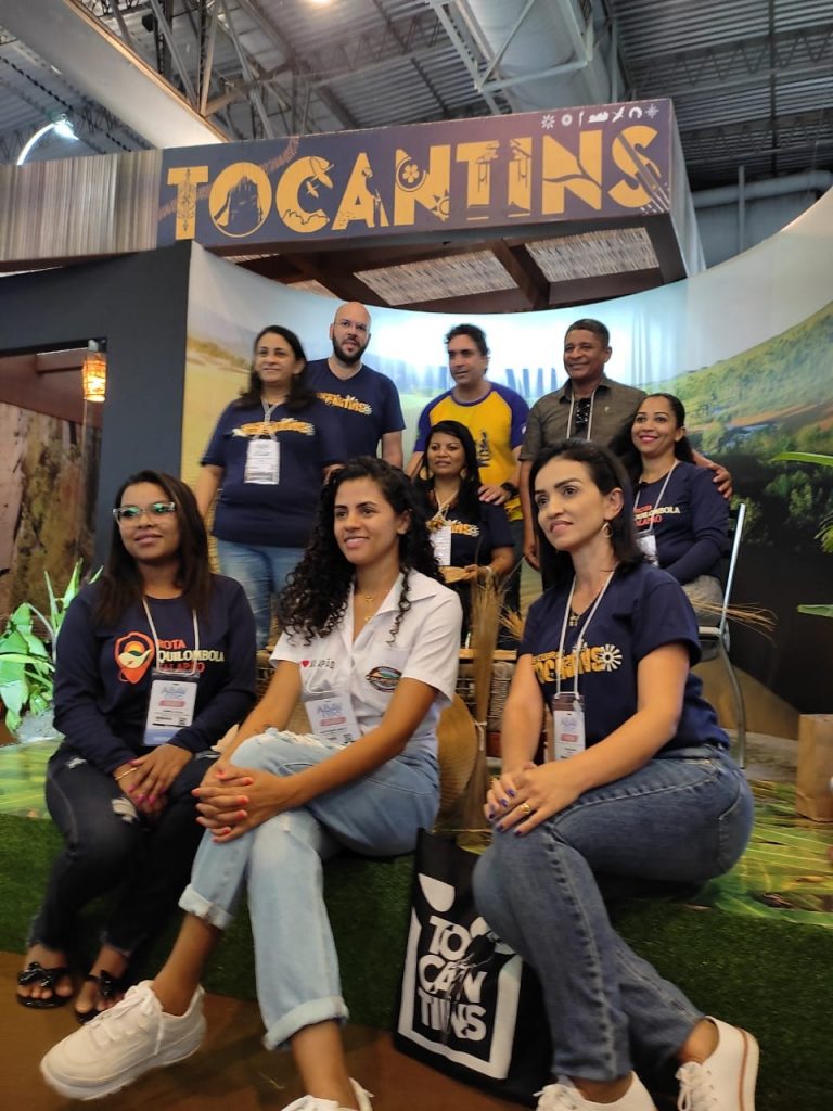 Portal Jaciara Barros – Alessandra Araújo posa para foto com um grupo no estande do Tocantins durante evento realizado em ambiente interno. – Portal Jaciara Barros