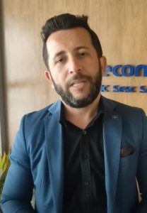 Portal Jaciara Barros – Homem de cabelo escuro e barba, veste blazer azul e está no Abav Expo 2022 diante de parede de madeira com letreiros. – Portal Jaciara Barros