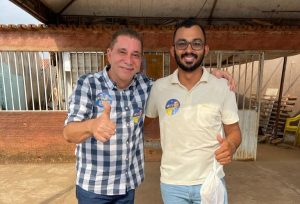 Portal Jaciara Barros – Homem de camisa xadrez faz sinal de positivo e exibe, ao ar livre, adesivos da campanha Palmas Que Te Acolhe. – Portal Jaciara Barros
