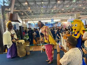 Portal Jaciara Barros – O público acompanha apresentações de trajes típicos na ABAV Expo 2022, entre estandes e pessoas registrando o evento. – Portal Jaciara Barros
