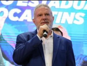 Portal Jaciara Barros – Mauro Carlesse, de terno azul, fala ao microfone diante de um painel colorido com textos do Senado ao fundo. – Portal Jaciara Barros