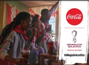 Portal Jaciara Barros – Três torcedores comemoram com garrafas de Coca-Cola em ambiente interno; logotipos da Copa do Mundo e da Coca-Cola à direita. – Portal Jaciara Barros