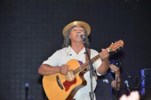 Portal Jaciara Barros – Homem de chapéu de palha canta e toca violão em festival em Tocantins, utilizando microfone à sua frente. – Portal Jaciara Barros