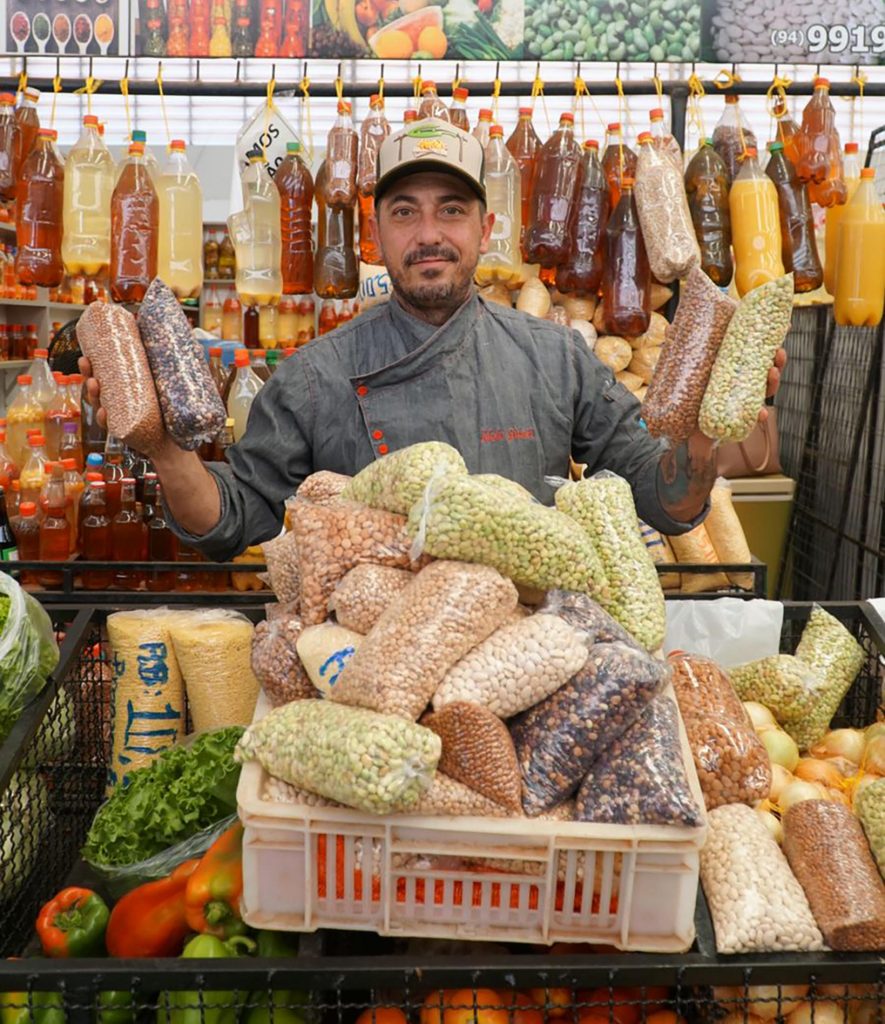 Portal Jaciara Barros – No Festival Gastronômico de Canaã dos Carajás, o chef Idolo Giusti está atrás de uma banca com sacos de feijão seco. – Portal Jaciara Barros