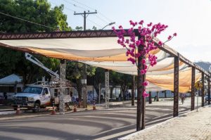 Portal Jaciara Barros – Funcionários instalam toldo de tecido em rua para o Festival Gastronômico de Taquaruçu; há caminhão e flores rosas no local. – Portal Jaciara Barros