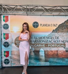 Portal Jaciara Barros – Giorgia de Bortoli, vestida de rosa claro, posa em frente ao banner do evento Harmonização Facial no Algarve. – Portal Jaciara Barros