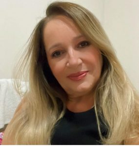 Portal Jaciara Barros – Josenete Fernandes, de cabelos loiros e blusa preta, sorri durante comemoração de aniversário em ambiente interno. – Portal Jaciara Barros