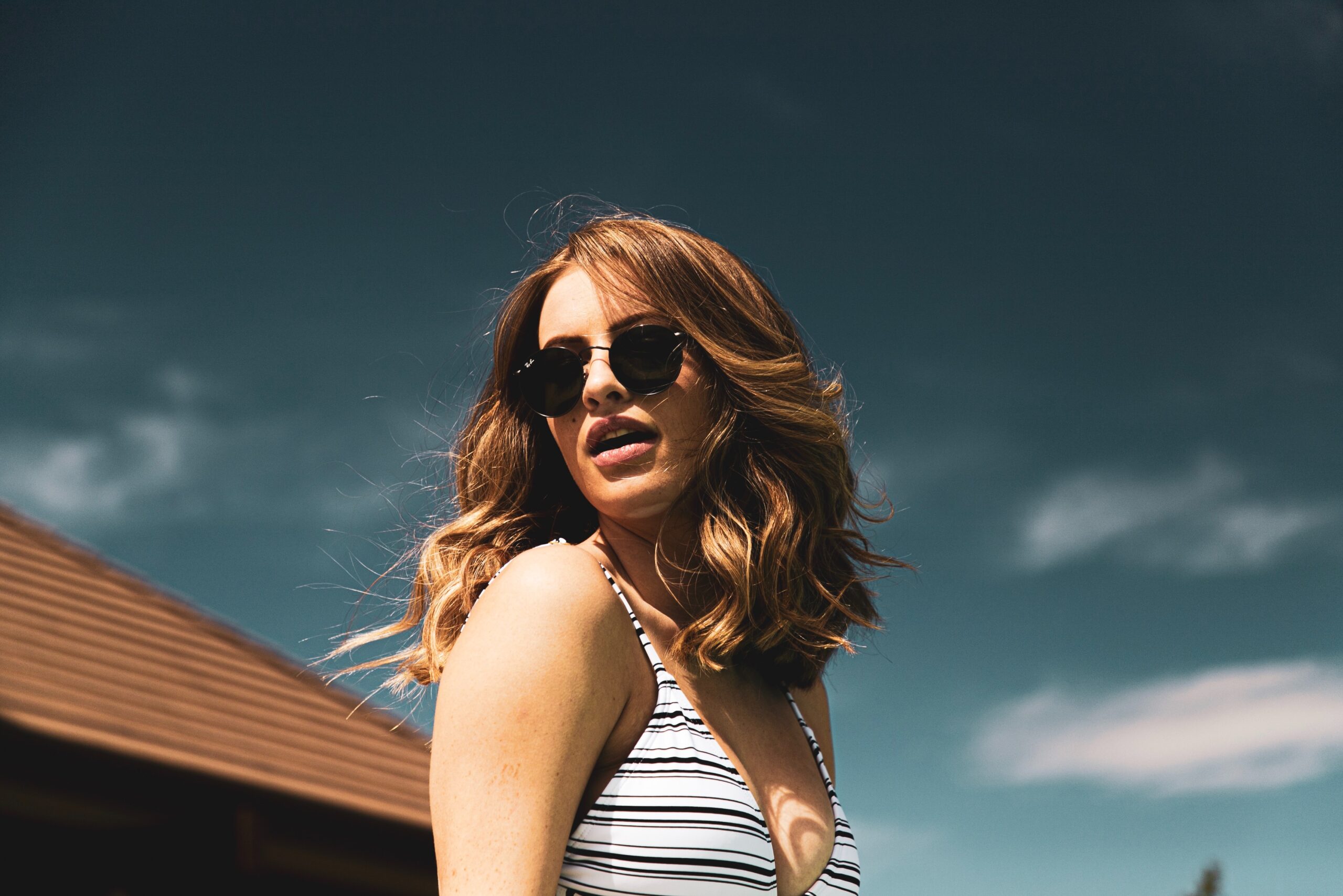 Por que meu cabelo não cresce? – Portal Jaciara Barros Portal Jaciara Barros – Mulher de cabelos ondulados, óculos escuros e blusa listrada posa ao ar livre, confiante apesar das preocupações capilares. – Portal Jaciara Barros