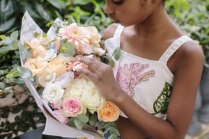 Portal Jaciara Barros – Jovem veste blusa branca PatBo e segura um buquê de flores em tons pastéis com folhas verdes. – Portal Jaciara Barros