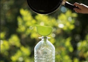 Portal Jaciara Barros – Durante o Festival Gastronômico de Taquaruçu, uma pessoa recicla óleo usado ao despejá-lo por um funil em uma garrafa ao ar livre. – Portal Jaciara Barros