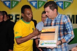 Portal Jaciara Barros – Dois homens apertam as mãos enquanto um entrega uma placa dos Jogos Mundiais Indígenas em reconhecimento ao incentivo esportivo. – Portal Jaciara Barros