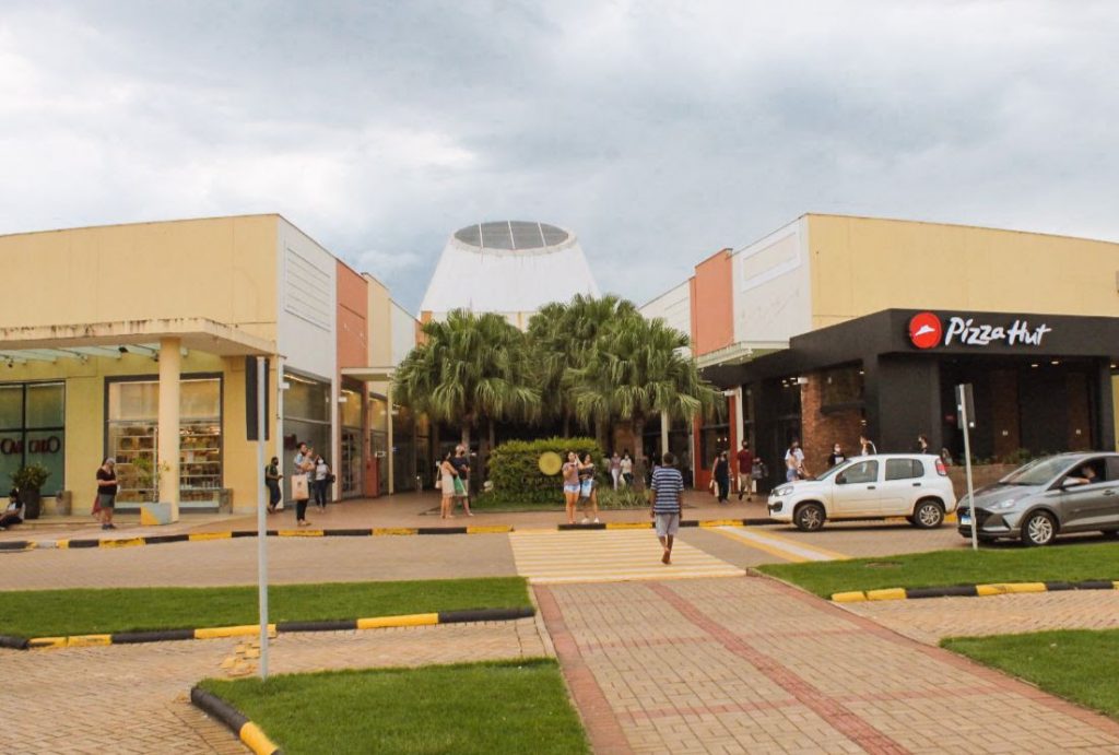Portal Jaciara Barros – Os clientes circulam em frente ao Capim Dourado Shopping, onde há palmeiras, carros estacionados e placa do Pizza Hut. – Portal Jaciara Barros