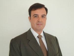 Portal Jaciara Barros – Homem de terno escuro, camisa branca e gravata marrom posa diante de fundo branco, representando mandatos coletivos. – Portal Jaciara Barros