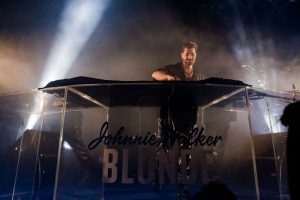 Portal Jaciara Barros – O DJ Alok se apresenta em um estande transparente da Johnnie Walker Blonde durante evento no Rio, sob luzes de palco. – Portal Jaciara Barros