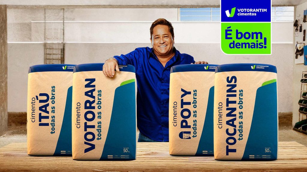 Portal Jaciara Barros – Homem sorri ao apresentar sacos de cimento com nova identidade visual, incluindo Votorantim Cimento, em oficina. – Portal Jaciara Barros