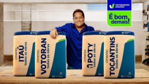 Portal Jaciara Barros – Homem sorri ao apresentar sacos de cimento com nova identidade visual, incluindo Votorantim Cimento, em oficina. – Portal Jaciara Barros