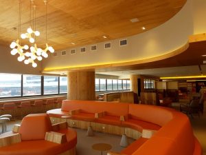 Portal Jaciara Barros – Espaço moderno com poltronas laranja, detalhes em madeira e grandes janelas, reservado para clientes VIP GOL ou do Programa de Fidelidade. – Portal Jaciara Barros