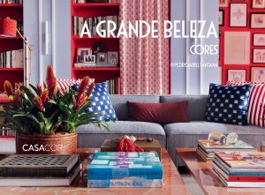 Portal Jaciara Barros – Uma sala de estar com um sofá cinza, almofadas coloridas e prateleiras vermelhas se destaca por sua paleta vibrante que lembra A Grande Beleza. – Portal Jaciara Barros