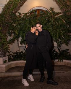 Portal Jaciara Barros – Mari Gonzalez e uma amiga posam usando looks pretos da Lacoste diante de um cenário com folhagem verde à noite. – Portal Jaciara Barros