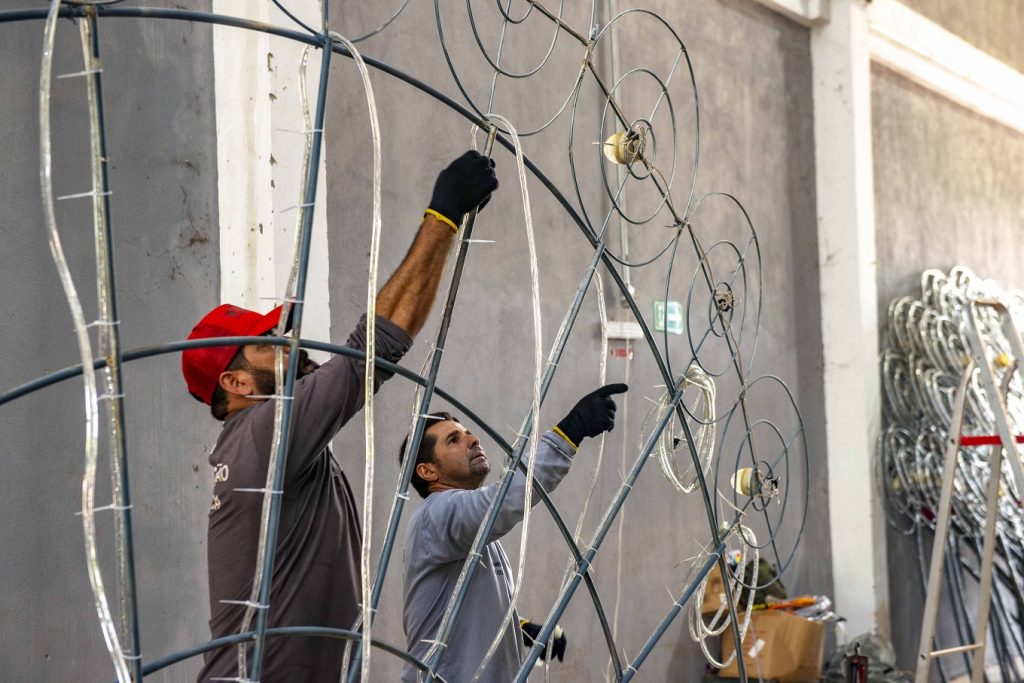 Portal Jaciara Barros – Trabalhadores montam estrutura metálica de túnel de luzes em Palmas, instalando decoração natalina em espaço coberto. – Portal Jaciara Barros