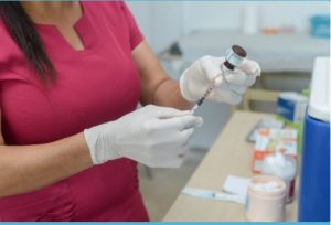 Portal Jaciara Barros – Profissional com luvas prepara seringa para vacinação no Shopping Capim Dourado, em ambiente médico. – Portal Jaciara Barros