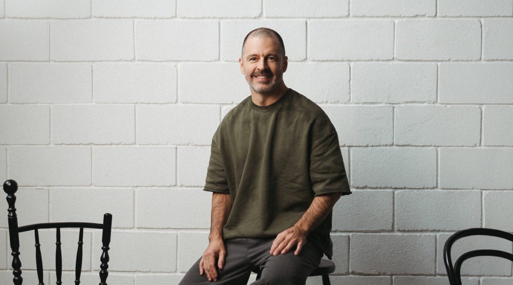 Maurício Arruda em palestra, com público atento em auditório contemporâneo iluminado em tons de verde e dourado.