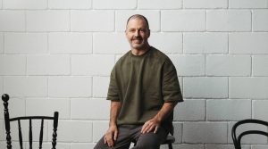 Maurício Arruda em palestra, com público atento em auditório contemporâneo iluminado em tons de verde e dourado.