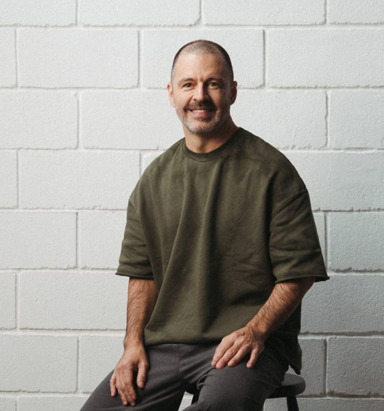 Maurício Arruda em palestra, com público atento em auditório contemporâneo iluminado em tons de verde e dourado.